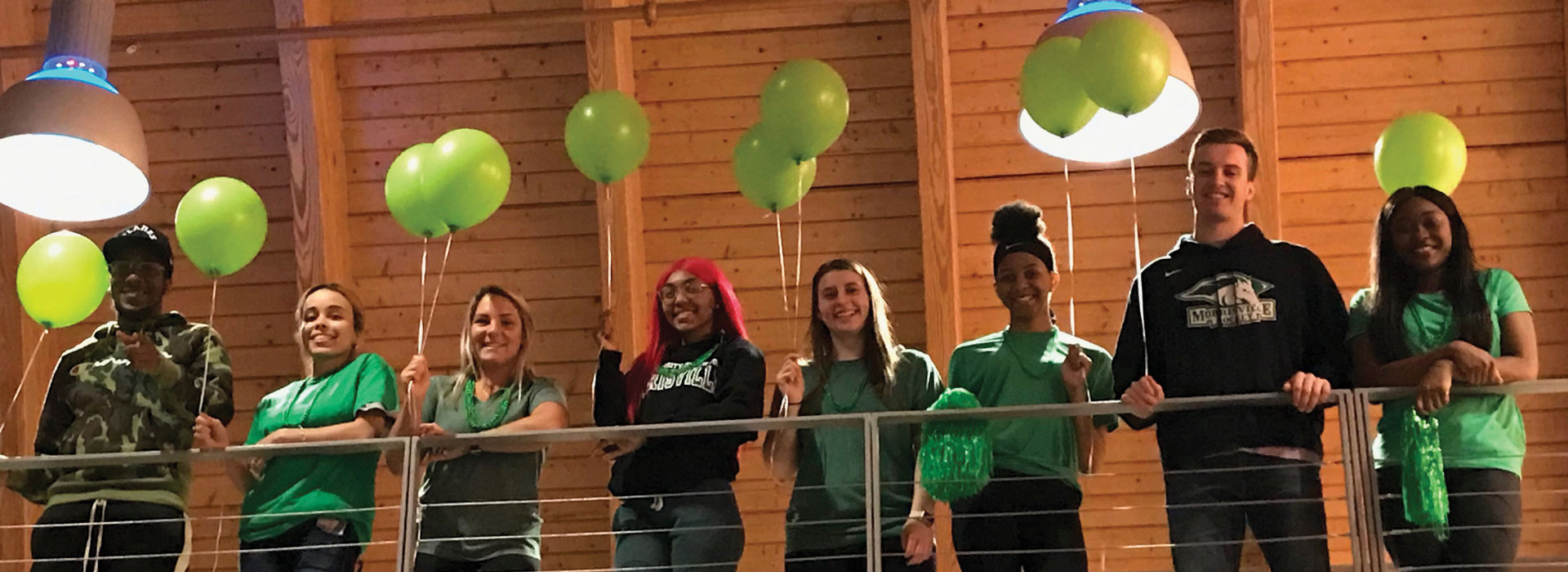 A group of students holding green balloons looking out over a railing
