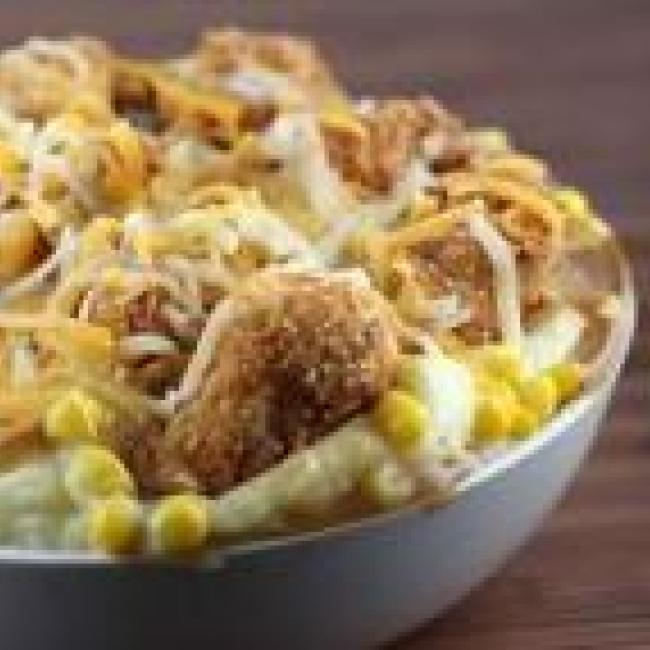 Mashed potatoes with chicken bites, corn, gravy, and cheese in a bowl